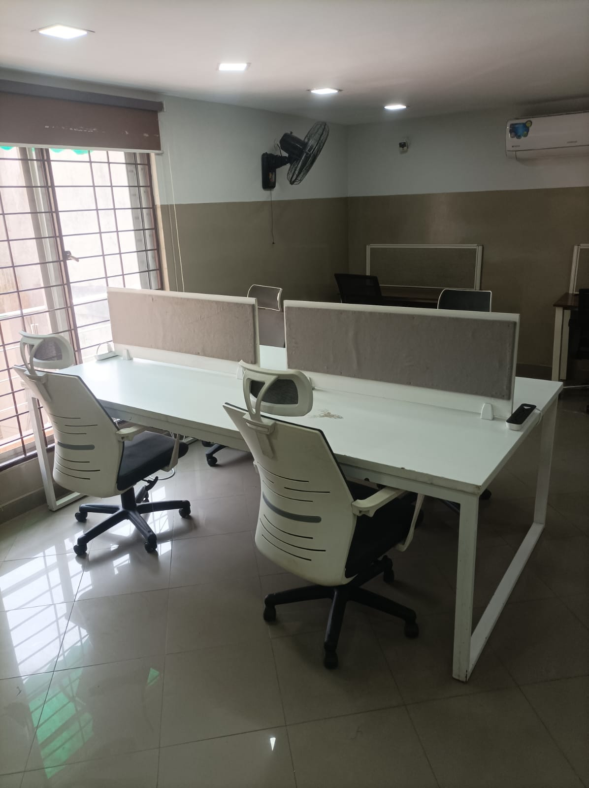 White 4-person collaborative island desks beside the window at KAMH coworking Lahore
